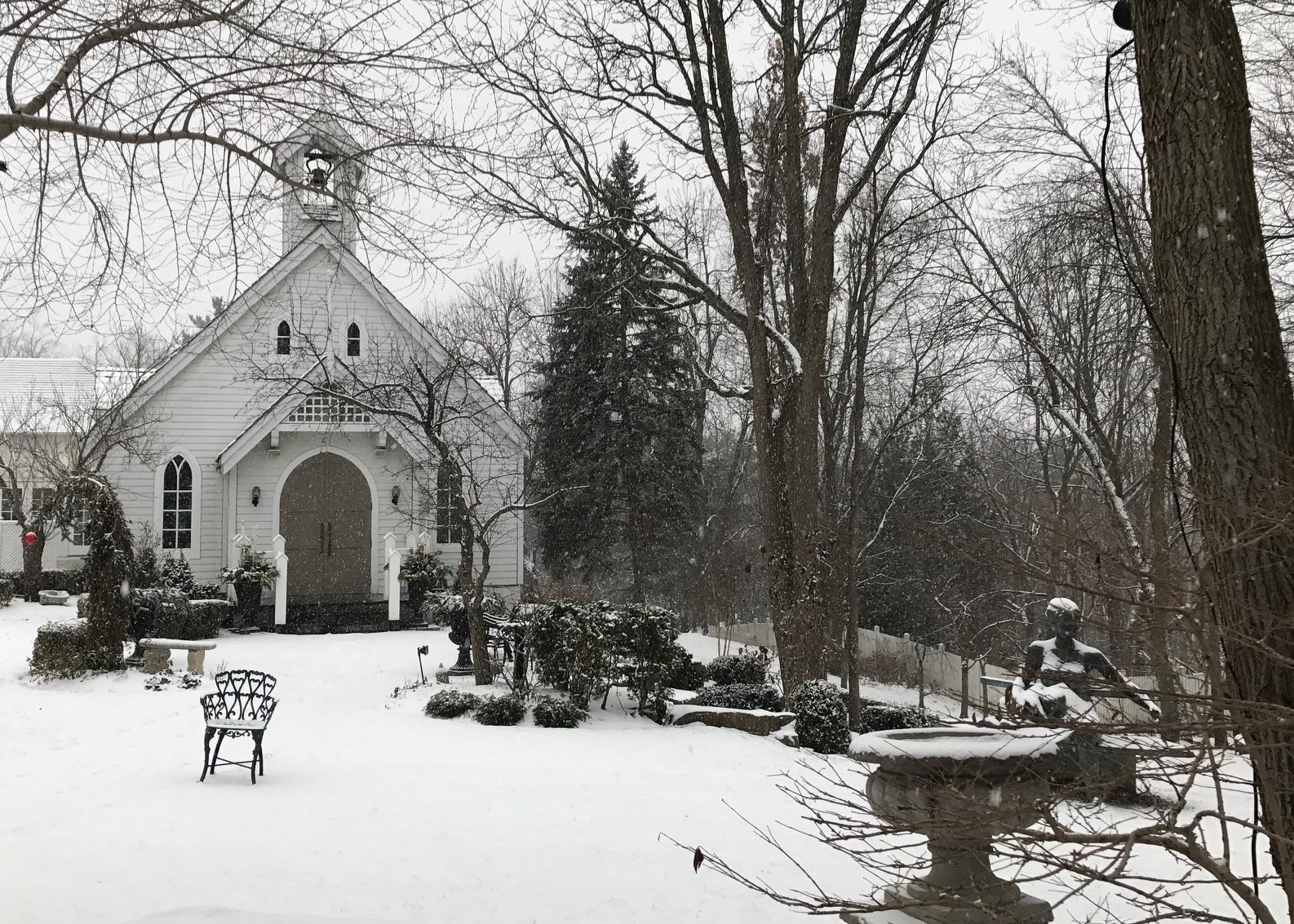 A black and white winter scene with a chapel in the background and trees in the foreground suggesting an older, simpler time.