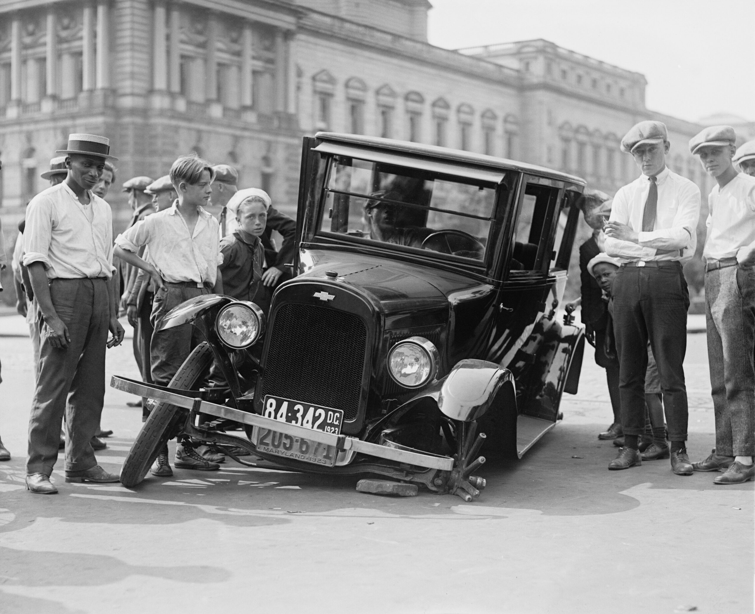 Damaged vintage car with men standing around it.