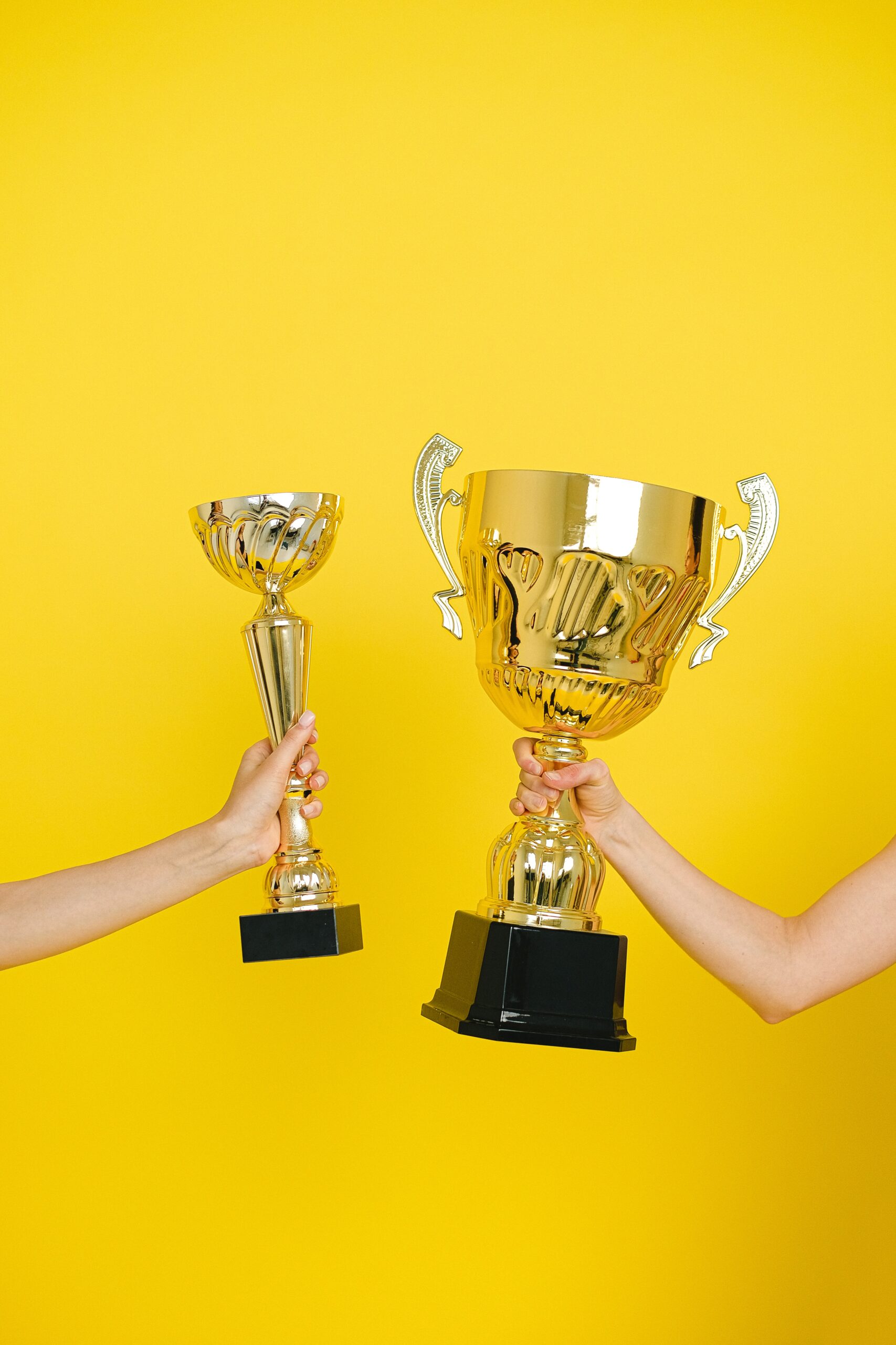 Two hands holding gold statuettes.