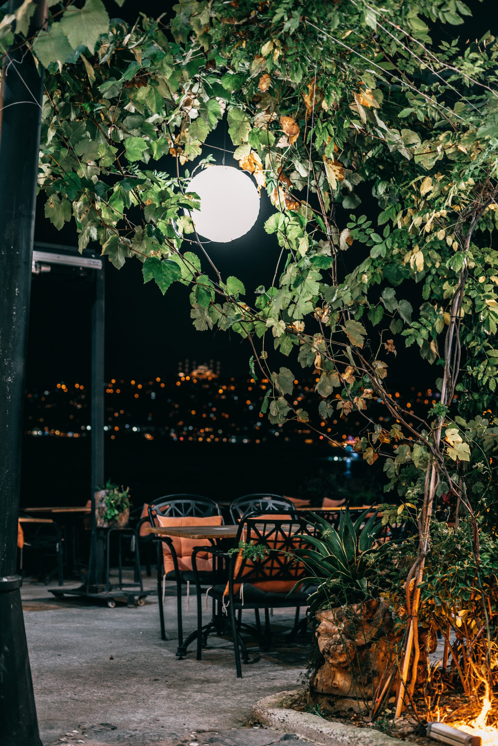 Patio cafe in a garden at night under a bright light.