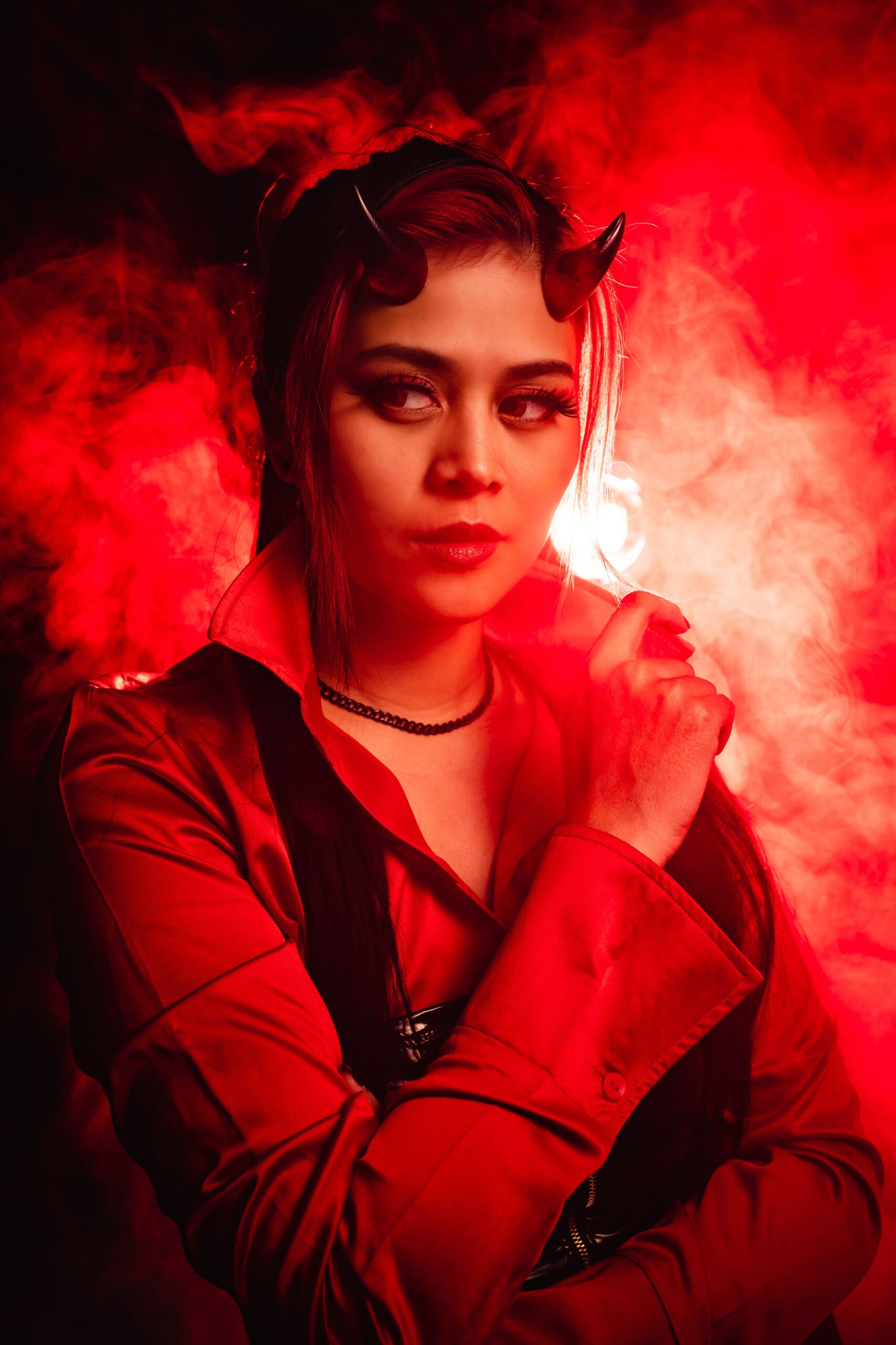 A woman in a devil costume with horns against a fiery red background.