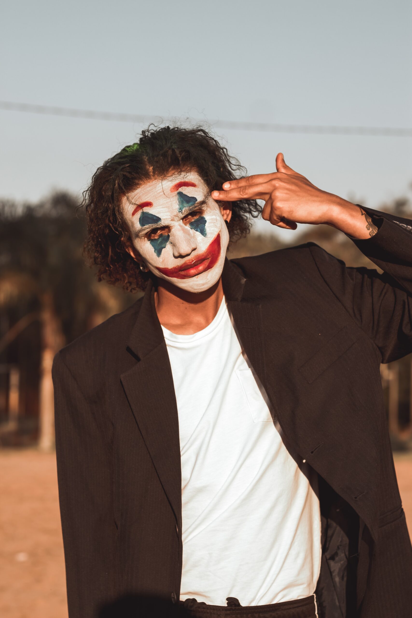 A sad looking clown making a gesture as if shooting himself in the head.