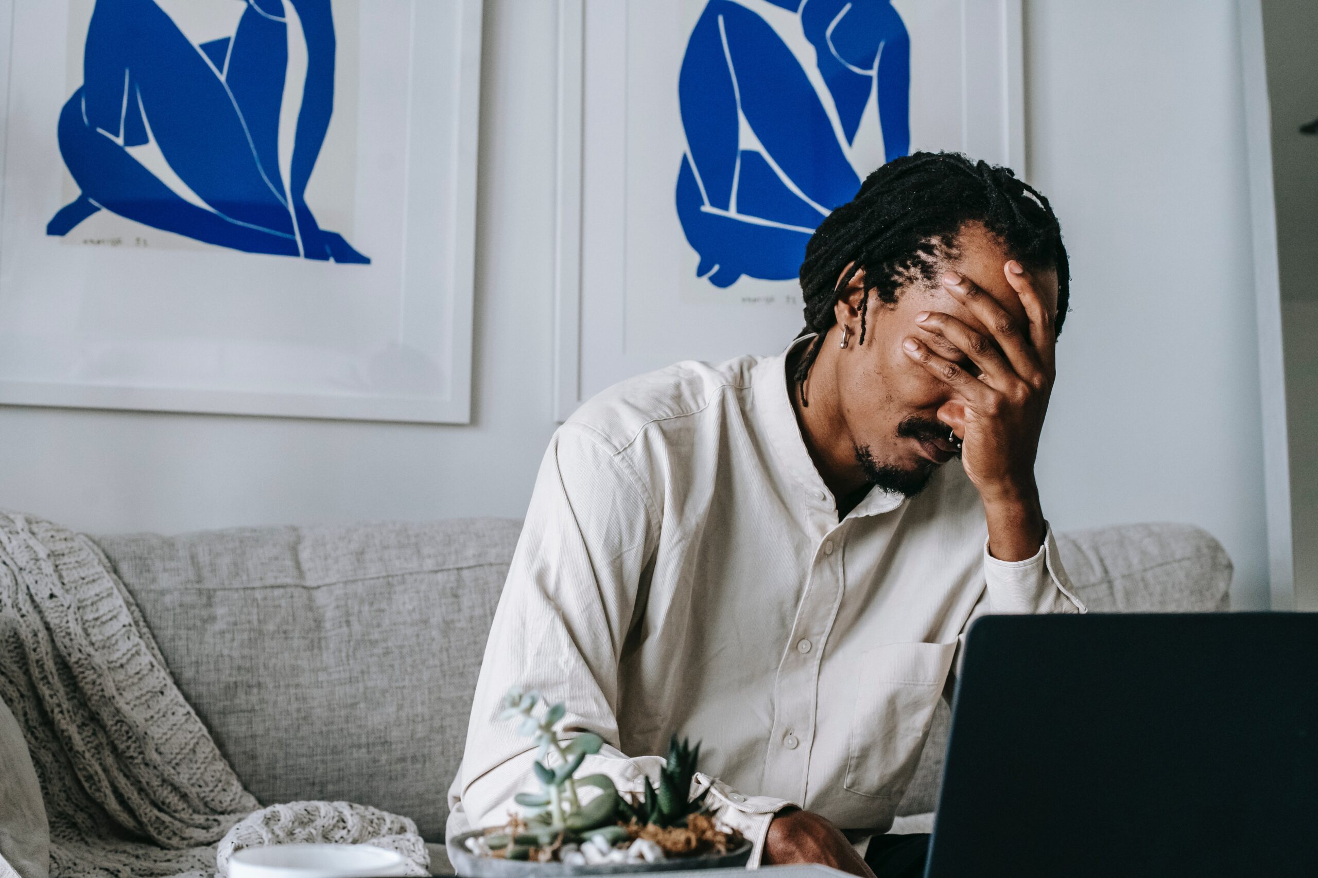 A man covering his face and looking upset while staring at his computer.