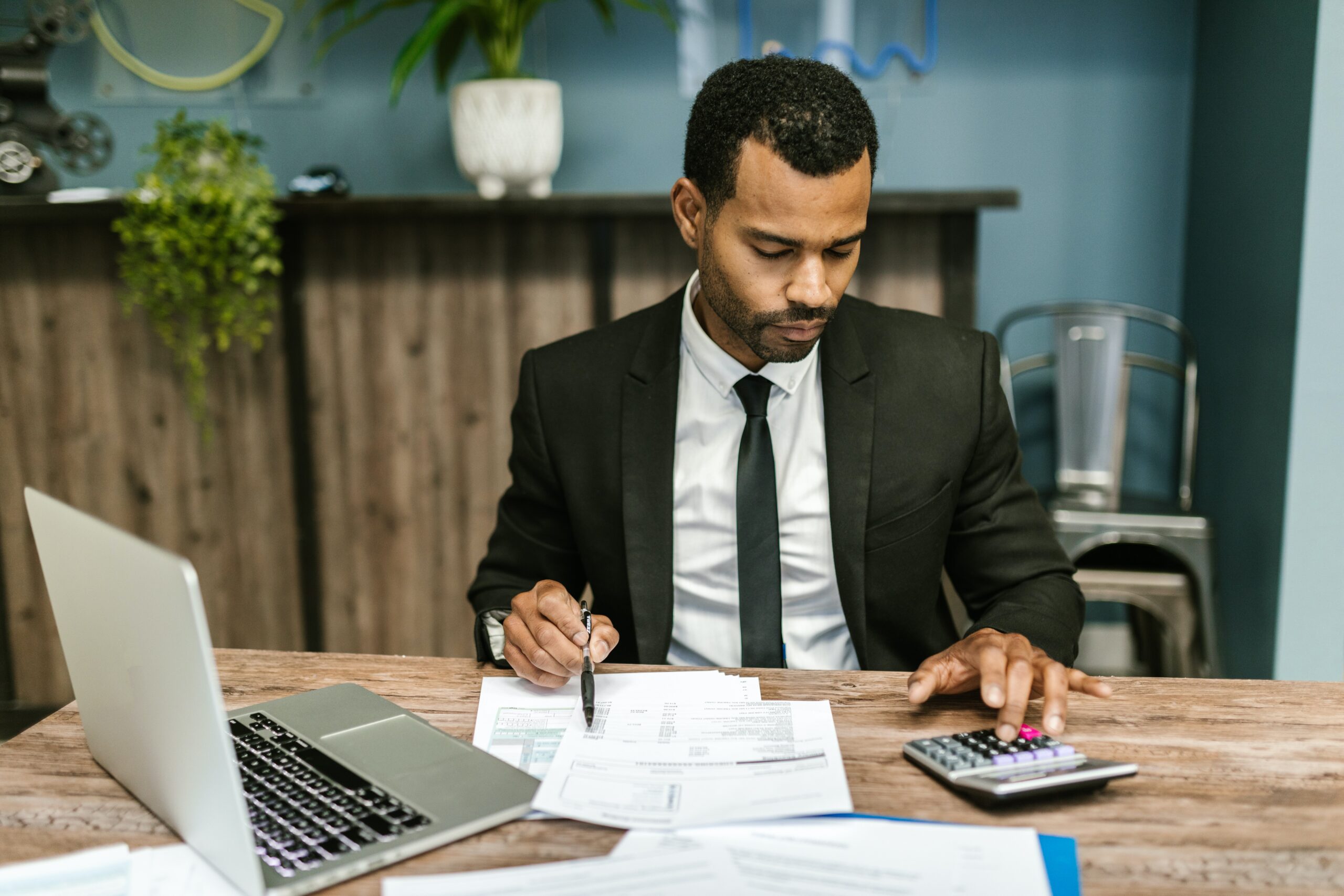 Man sitting at desk working with a laptop and a calculator.