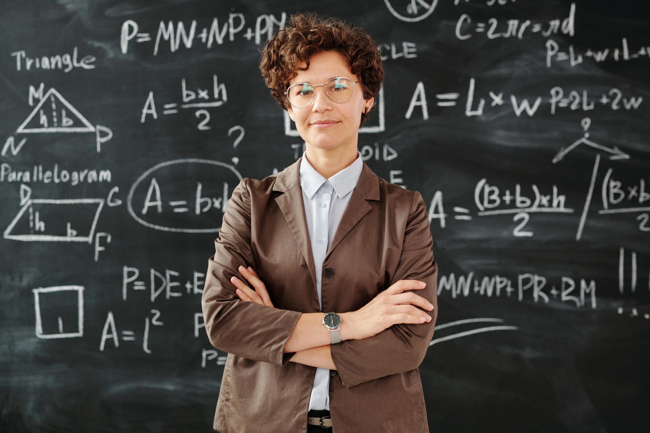 Female teacher standingi in front of blackboard filled with mathematical equations.