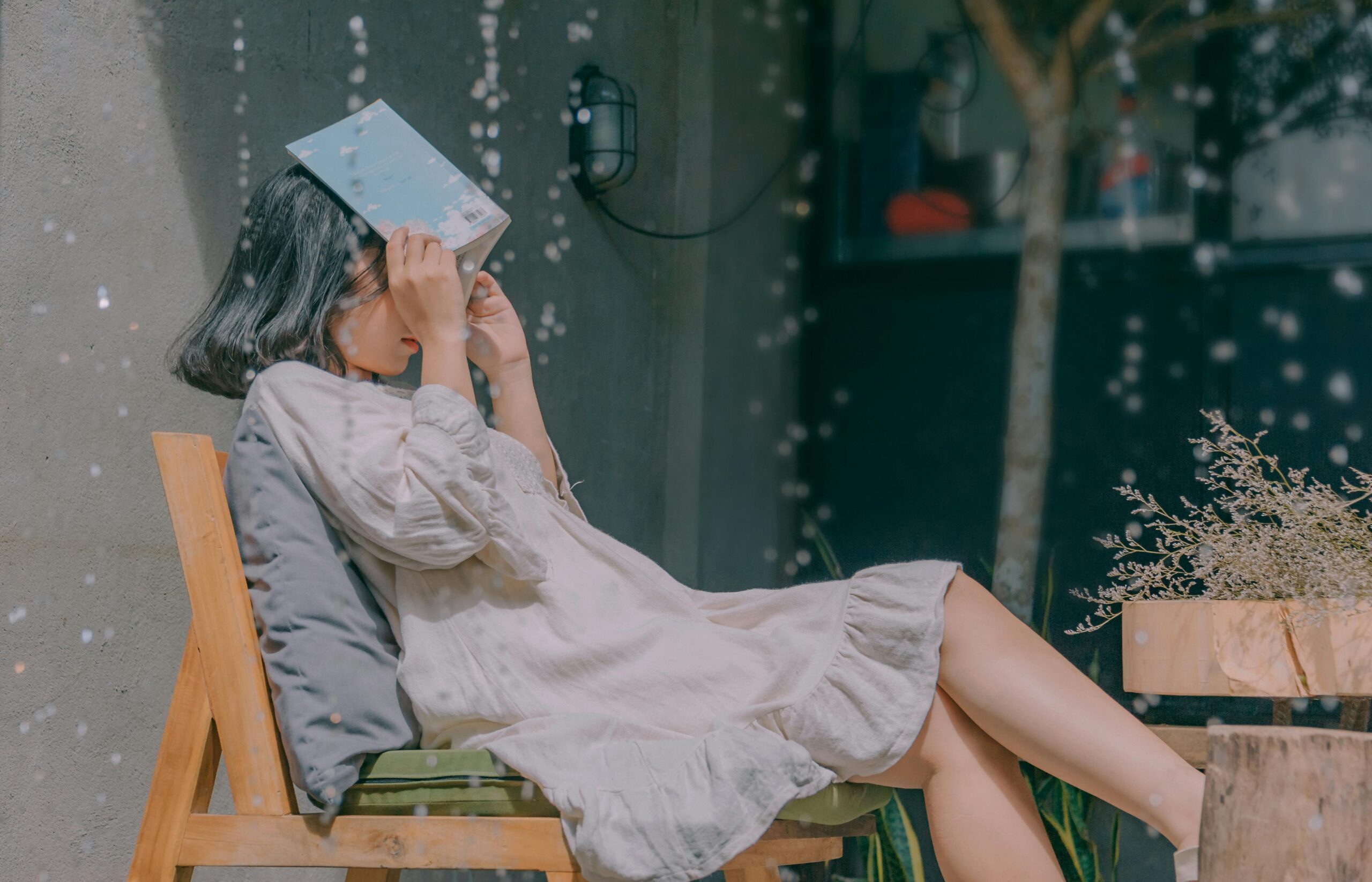 Woman sitting in the rain with a book over her head.