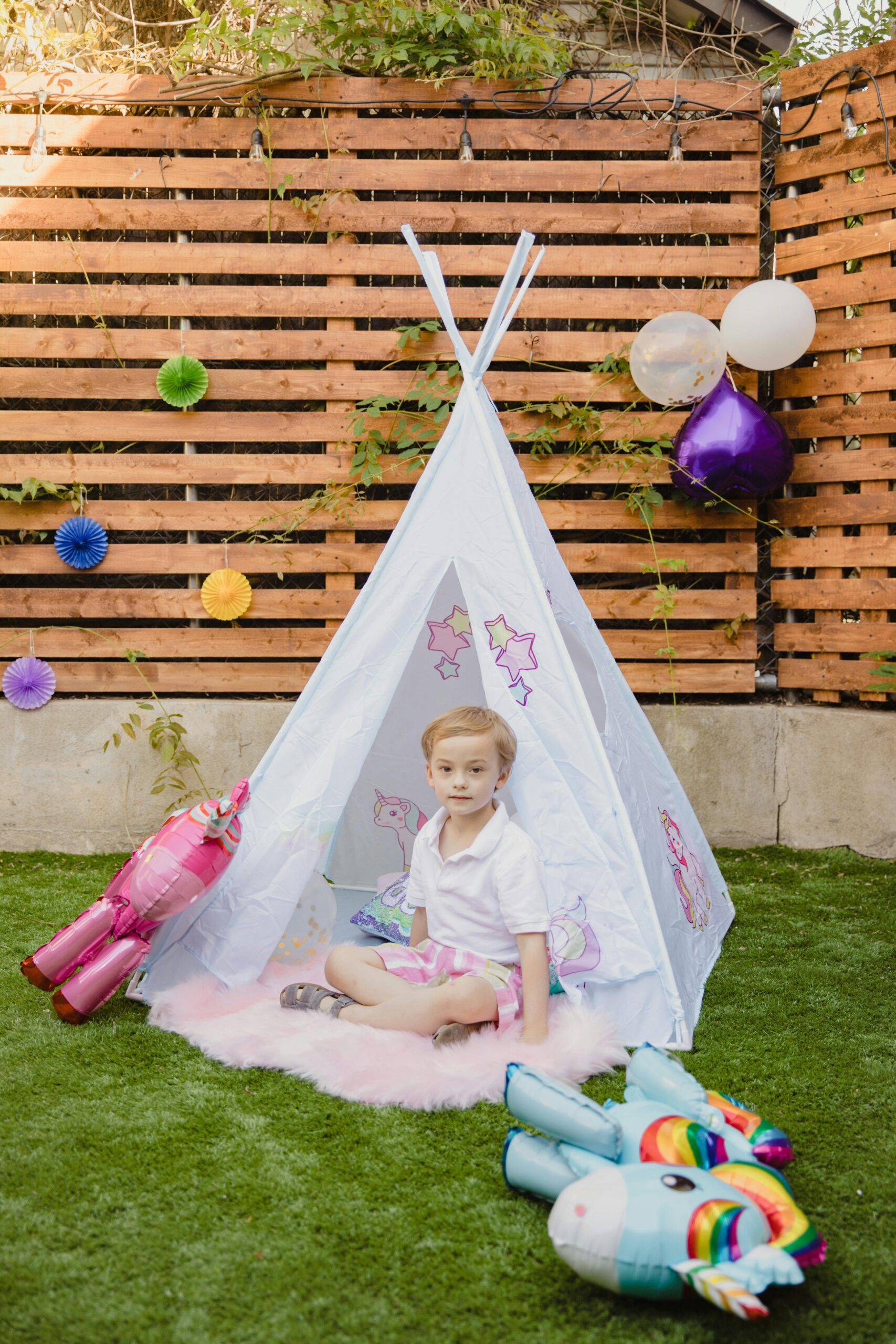 A child sitting in a child's tent with balloons and a toy unicorn.