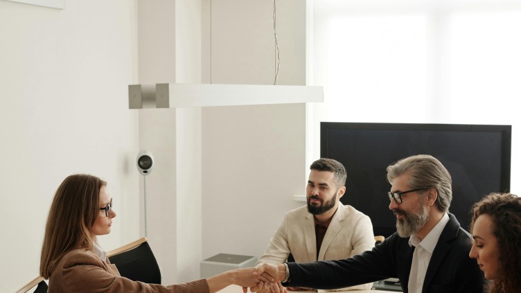 Group of business people at a boardroom table, two of whom are shaking hands.